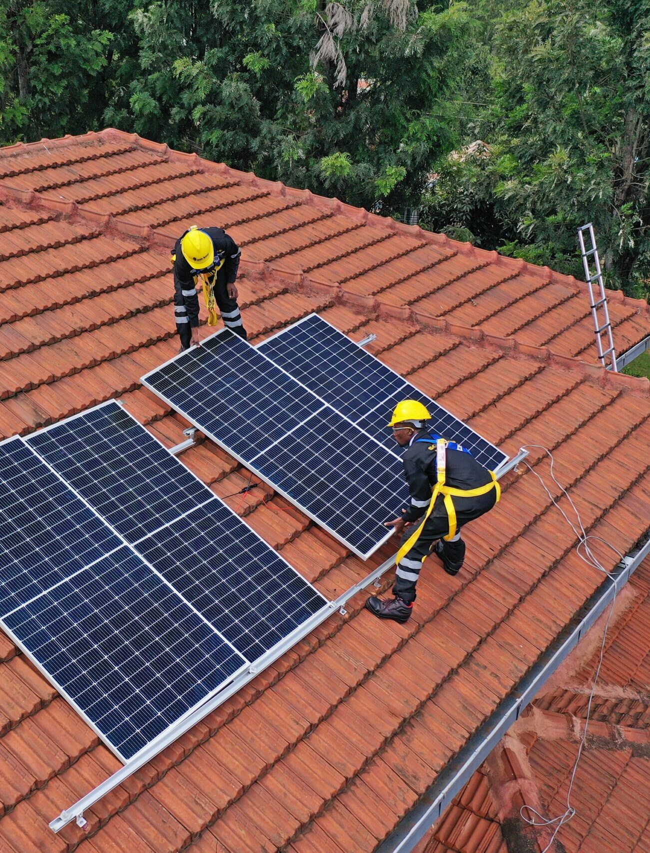 Image shows two Sun King employees wearing PPE installing solar panels on the roof of a house.