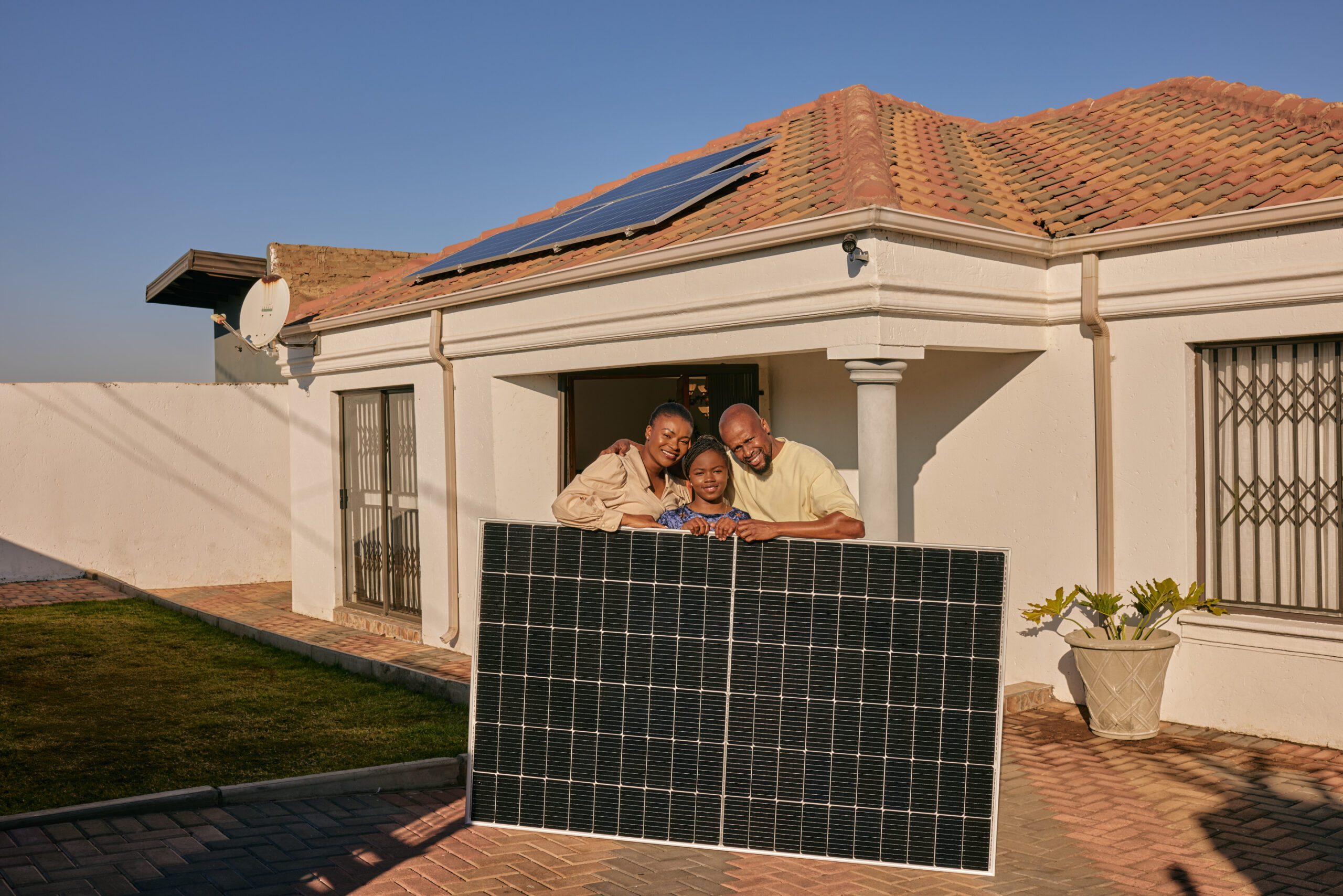 Family poses outside their house with a solar panel, which is part of Sun King's powerful rooftop solar inverter systems.